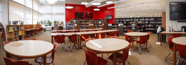 A spacious library featuring tables and chairs arranged for reading and studying, surrounded by shelves of books.