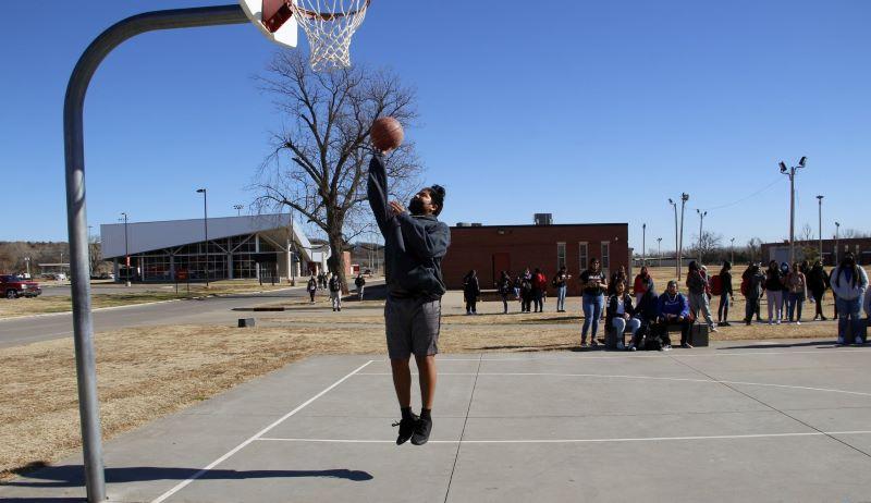 Student putting basketball in net on basketball court.