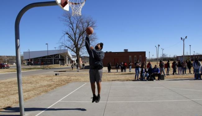 Student putting basketball in net on basketball court.
